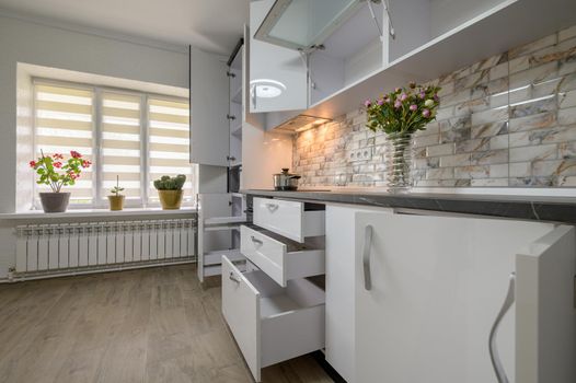 Interior renovation showcase of well designed modern trendy white kitchen, cabinet doors open, drawers retracted