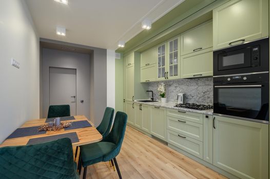 Modern trendy light green luxurious kitchen with dining table and dark green chairs