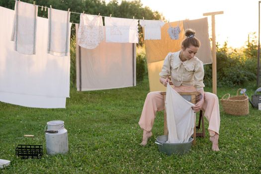 Laundry day. A woman hangs linen and towels on a tree in the courtyard of a village house. Summer cottage concept.