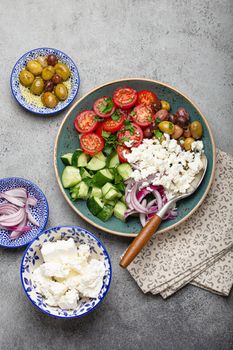 Greek mediterranean salad with tomatoes, feta cheese, cucumber, whole olives and red onion in blue ceramic plate on gray concrete background from above, traditional appetizer of Greece