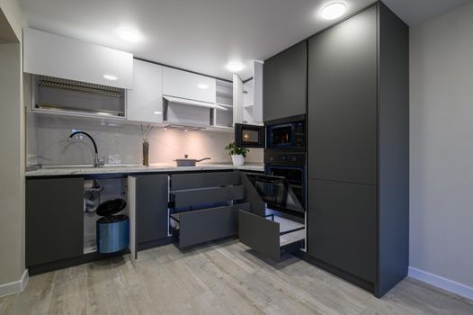 Showcase interior of modern simple dark grey and white kitchen, drawers retracted, doors open