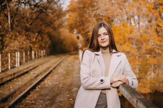 A beautiful long-haired woman walks through the autumn streets. Railway, autumn leaves, a woman in a light coat.