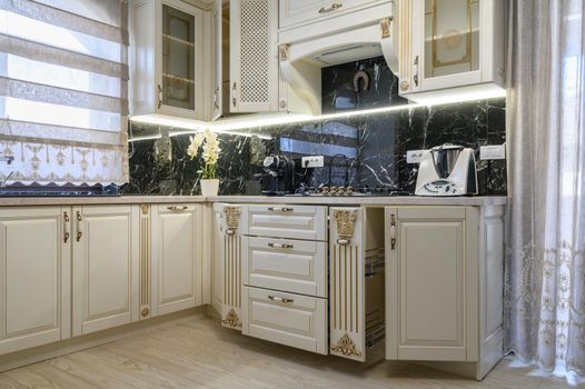 White rich classic cozy kitchen and dining room in city house interior, some drawers are open