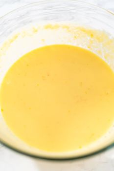 Mixing wet ingredients in a large glass mixing bowl to bake mini Easter bread kulich.