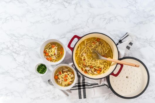 Flat lay. Serving chicken noodle soup with kluski noodles in white ceramic soup bowls.