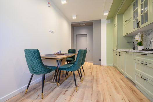 Modern trendy light green luxurious kitchen with dining table and dark green chairs