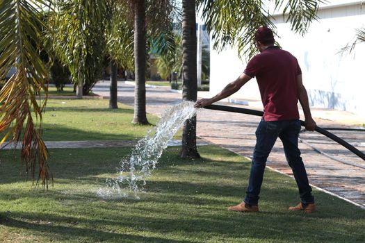 santana, bahia, brazil - september 13, 2022: gardener pours water with a hose in a garden of a public square in the city of Santana.
