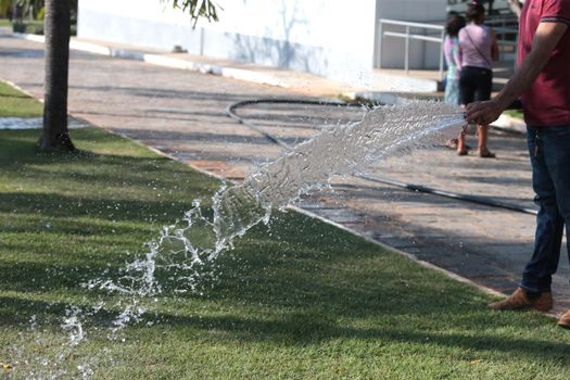 santana, bahia, brazil - september 13, 2022: gardener pours water with a hose in a garden of a public square in the city of Santana.