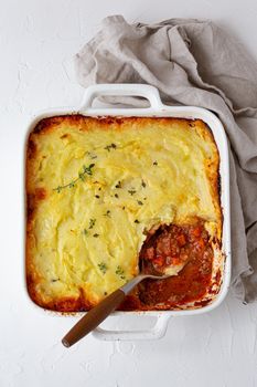 Traditional dish of British cuisine Shepherd's pie casserole with minced meat and mashed potatoes in ceramic baking dish on white rustic table with spoon from above