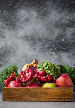 Selection of fresh fruit, greens, vegetables in wooden tray on grey stone background table, detox, diet, clean eating, vegetarian, healthy food concept, space for text.