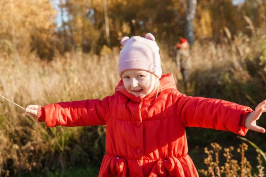 A little girl in a red coat walks in nature in an autumn grove. The season is autumn.