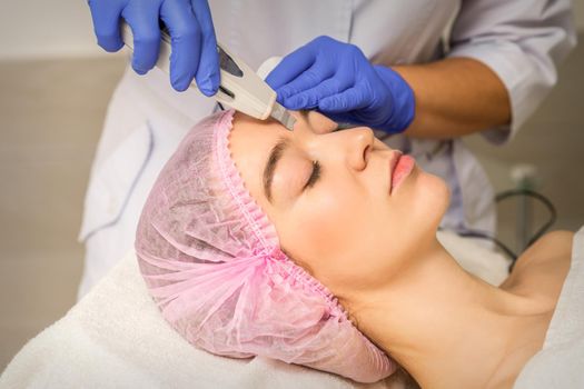 Young caucasian woman having ultrasonic peeling with ultrasound device in a cosmetic beauty salon