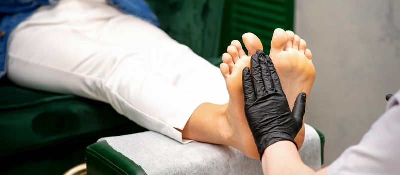Moisturizing the feet. Hands of pedicure master in black gloves care about female feet. Foot massage. Pedicure beauty salon concept