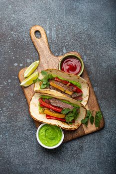 Traditional Mexican dish Beef fajitas tacos served on wooden cutting board with tomato salsa and guacamole on rustic stone background from above, American Mexican food