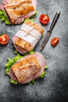 Fresh ciabatta sandwiches with ham, cheese, lettuce, tomatoes on stone concrete background, close-up, top view. Making healthy sandwiches for snack or lunch concept