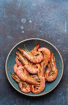 Whole fried big shrimps with seasonings in blue bowl on stone rustic background from above. Fresh cooked delicious grilled shrimps served on plate top view, healthy seafood meal. Space for text