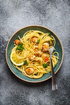 Spaghetti with seafood, delicious fried cooked scallops served on blue plate, grey rustic concrete background, top view, close-up. Seafood pasta concept