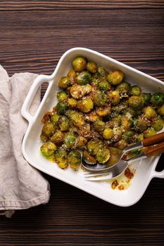 Healthy vegetarian dish roasted brussels sprouts with butter and parmesan cheese in white ceramic casserole top view on dark rustic wooden table from above, vegan food