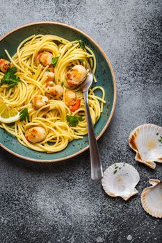 Spaghetti with seafood, delicious fried cooked scallops served on blue plate, grey rustic concrete background, top view, close-up. Seafood pasta concept