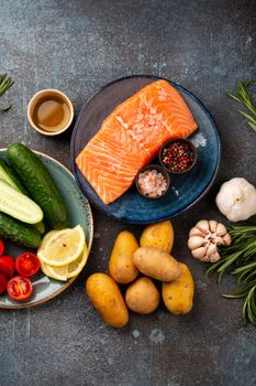 Raw salmon fish fillet, fresh vegetables, herbs - ingredients for cooking healthy meal. Natural clean organic healthy food selection on concrete background, dieting and nutrition concept. Top view