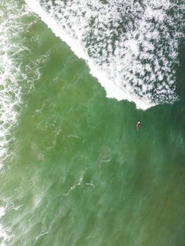 An overhead drone shot of a surfer in the wavy sea, Murtosa, Aveiro - Portugal.