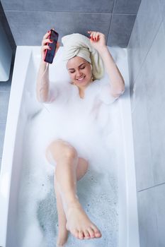 Beautiful young woman listens to music with headphones and sings while taking a bath at home. Relax after a hard day. Relaxing spa treatment.
