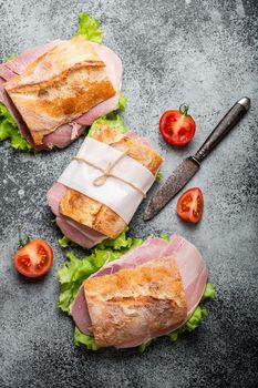 Fresh ciabatta sandwiches with ham, cheese, lettuce, tomatoes on stone concrete background, close-up, top view. Making healthy sandwiches for snack or lunch concept