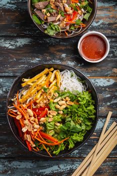 Asian, Chinese or Vietnamese style noodles salad with fresh vegetables, fried tofu and peanuts, served in rustic ceramic bowl on colorful wooden background. Healthy diet clean eating or vegan concept