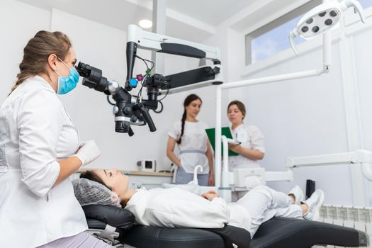 Female dentist using dental microscope treating patient teeth at dental clinic office. Medicine, dentistry and health care concept