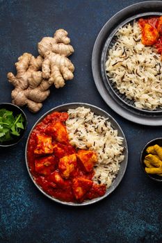 Chicken tikka masala dish with rice, flat Indian bread and spices in rustic metal plates on concrete background top view. Chicken tomato curry, turmeric root, fresh cilantro, traditional Indian meal