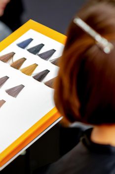 Young caucasian woman choosing a color from the hair color chart in a beauty salon