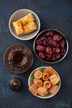 Traditional Arab fresh hot tea time with sweets, baklava, dates, lokum from above. Ramadan snack with Turkish delights and Arabic pastry on blue rustic background top view.