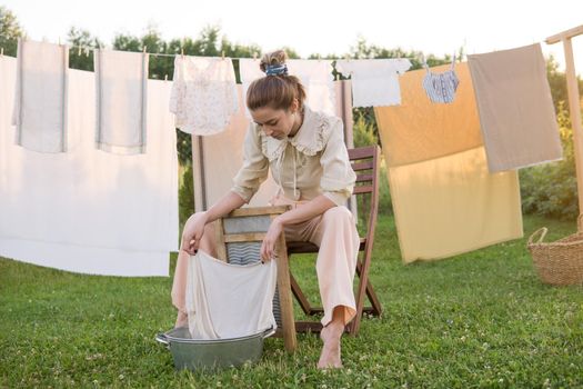 Laundry day. A woman hangs linen and towels on a tree in the courtyard of a village house. Summer cottage concept.