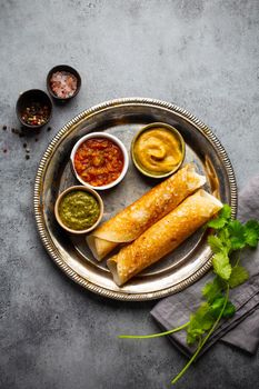 Traditional Indian rice pancakes Dosa with different dips chutney and seasonings on rustic metal plate on stone background table. Quick meal or vegetarian snack of South India, top view