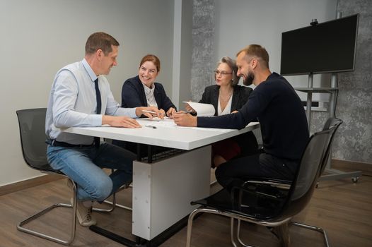 Four colleagues are discussing blueprints in a conference room in an office. Brainstorming of engineers and architects