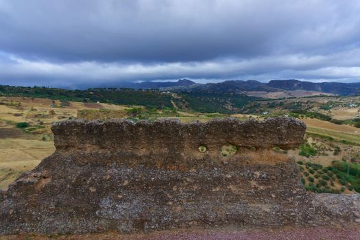 close-up of the remains of the old city wall of Ronda, Malaga, Spain, with mountainous landscape in the background.