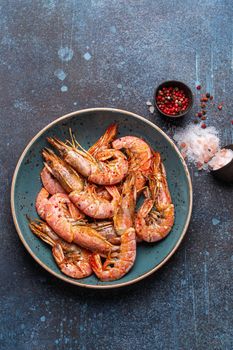 Whole fried big shrimps in blue bowl with salt and pepper on stone rustic background from above. Fresh cooked delicious grilled shrimps served on plate top view, healthy seafood meal