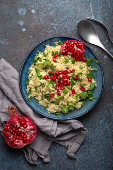 Bright colourful couscous or bulgur salad with pomegranate seeds Tabbouleh in rustic blue ceramic bowl top view on concrete background, traditional middle eastern or arab dish.