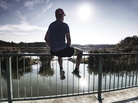 Sportsman is sitting on handrail in the park. Feet of jogging man.  Sunny morning, sport concept