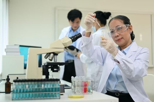 Smiling middle aged scientist working analysis with liquid test tube in the science research laboratory.