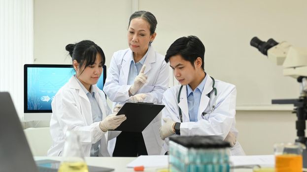 Senior female scientist and young laboratory assistants analyzing and summarising information for scientific report.