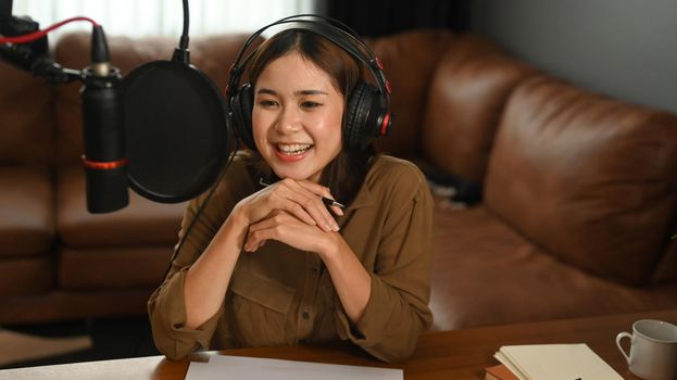 Smiling female host wearing headphones and recording podcast at broadcast studio. Communication and technology concept.