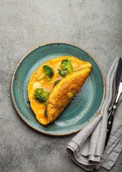 Healthy vegetarian egg omelette with green broccoli folded in half served on plate with fork and knife top view on gray stone concrete background table, diet and healthy clean eating concept