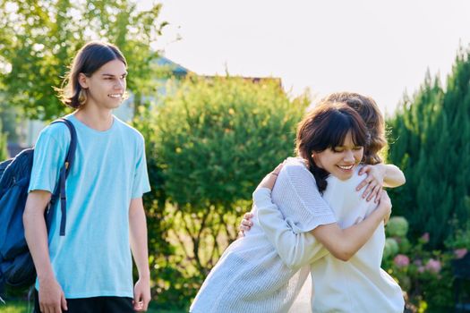 Meeting of three teenage friends, outdoor on a sunny day. Teenagers 17, 18 years old hugging, rejoicing, greeting, communication lifestyle friendship youth concept