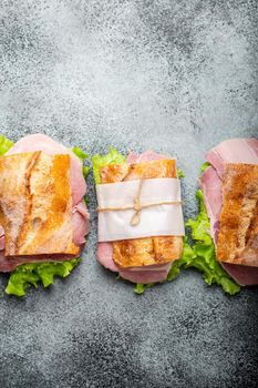 Fresh ciabatta sandwiches with ham, cheese, lettuce on stone concrete background, close-up, top view. Making healthy sandwiches for snack or lunch concept