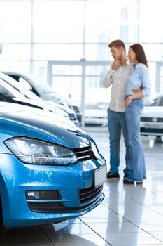 Looking for the perfect car. Selective focus on a car young couple choosing a car to buy at the car salon on the background