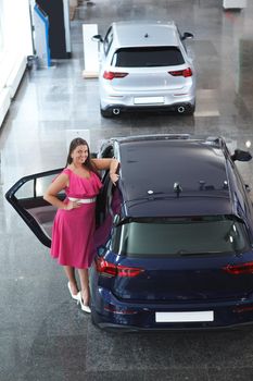 Vertical full length shot of a happy female customer standing near her new car at the dealership