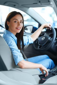 Classy driver. Shot of an attractive woman smiling to the camera over her shoulder while sitting in a new car at the car salon