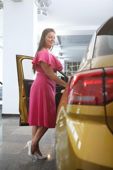Vertical full length shot of a happy woman examining car for sale at dealership