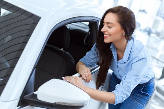 Can see myself on the road already. Portrait of a beautiful smiling woman looking inside the new car at the car salon